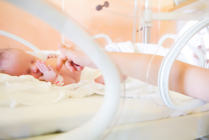 Madre acariciando a su bebé prematuro en la incubadora