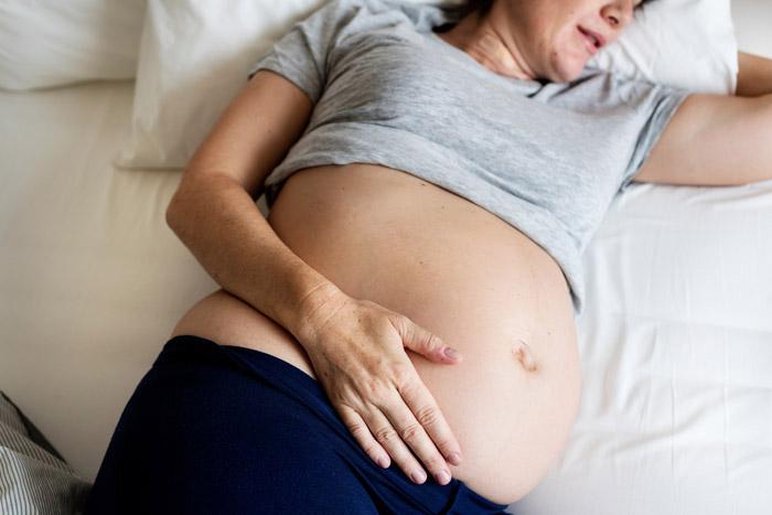 Mujer embarazada tumbada en la cama sintiendo cómo se mueve su bebé