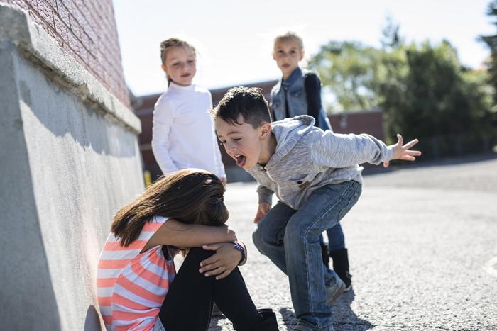 Grupo de niños en el colegio acosando a una niña que está sentada en el suelo 