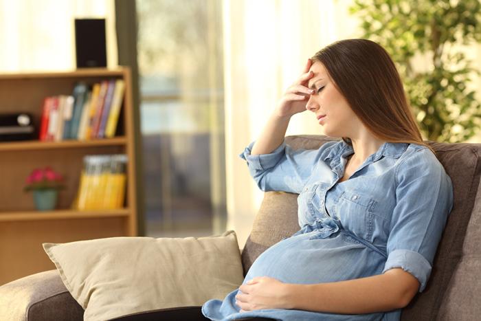 Mujer embarazada con cefalea en el sofá