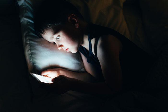 Niño mirando el móvil en la cama antes de dormir