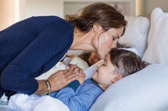  Madre besando en la frente y dando las buenas noches a su hijo en la cama