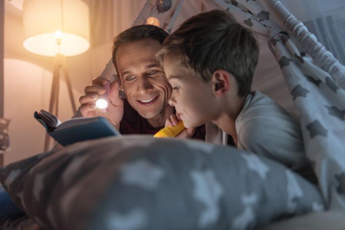 Padre e hijo leyendo cuentos en la cama con linternas