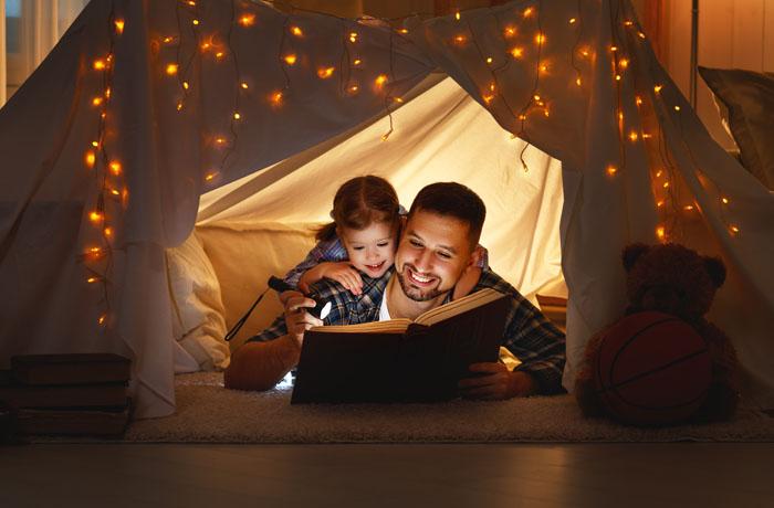 Padre e hija leyendo un cuento con una linterna en una tienda de campaña en casa