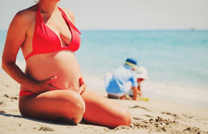 Mujer embarazada con un bikini rojo en la playa