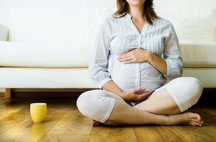 Mujer embarazada sentada en el suelo junto a una taza