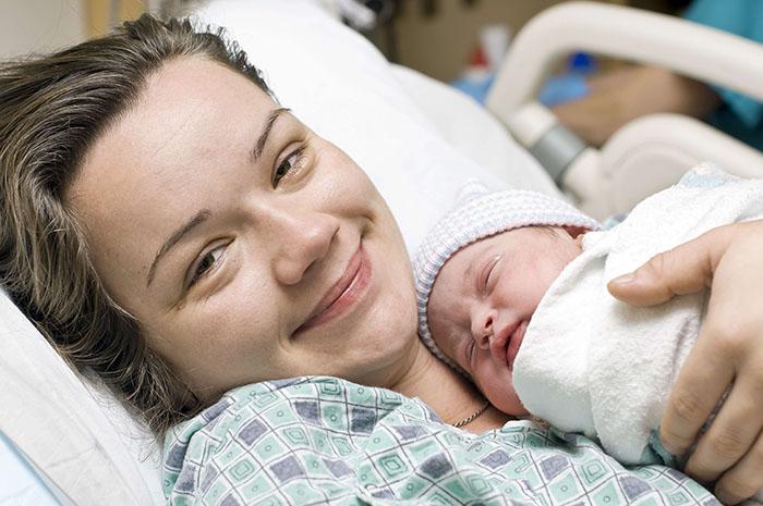 Mujer sonriente tras el parto sosteniendo a su bebé