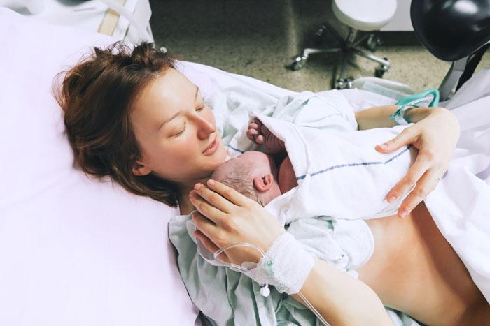 Mujer sosteniendo a su bebé al poco de nacer en el hospital