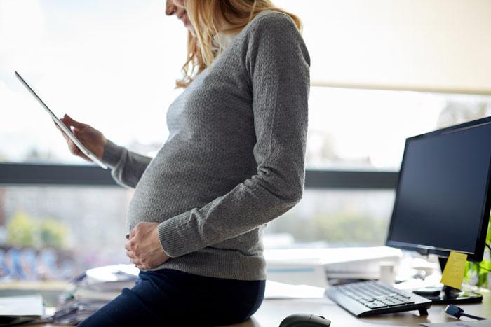 Mujer embarazada mirando una tablet en la oficina