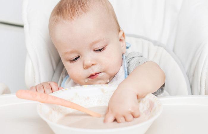 Bebé metiendo la mano en un plato de papilla con cereales