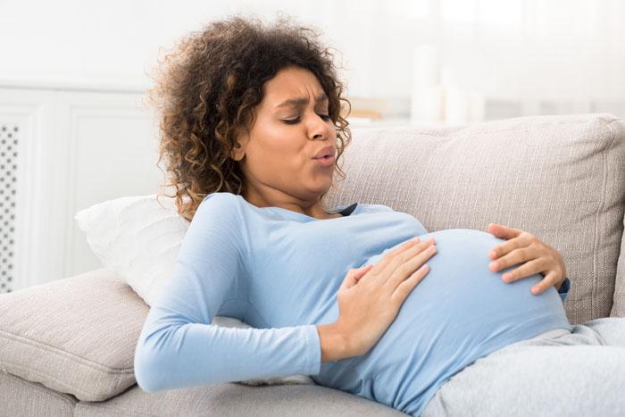 Mujer embarazada tumbada en el sofá con contracciones y respirando