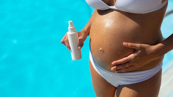 Mujer embarazada poniéndose crema protectora para tomar el sol en la piscina