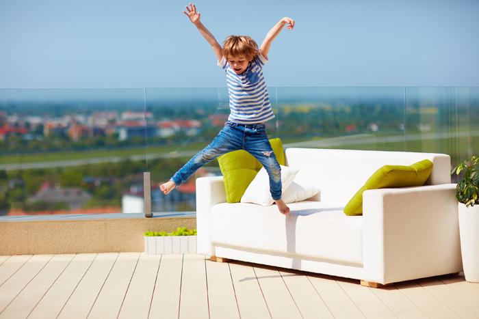 Niño saltando al sol en el sofá de una terraza