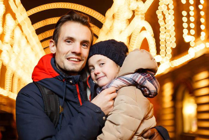 Padre e hija abrazados en una calle iluminada en Navidad