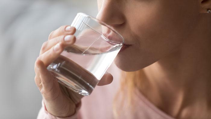 Mujer bebiendo agua en un vaso de cristal