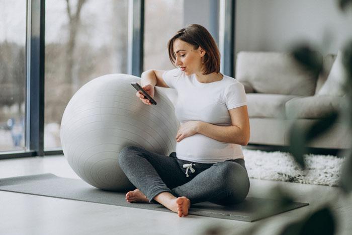 Mujer embarazada haciendo yoga en casa con una app móvil