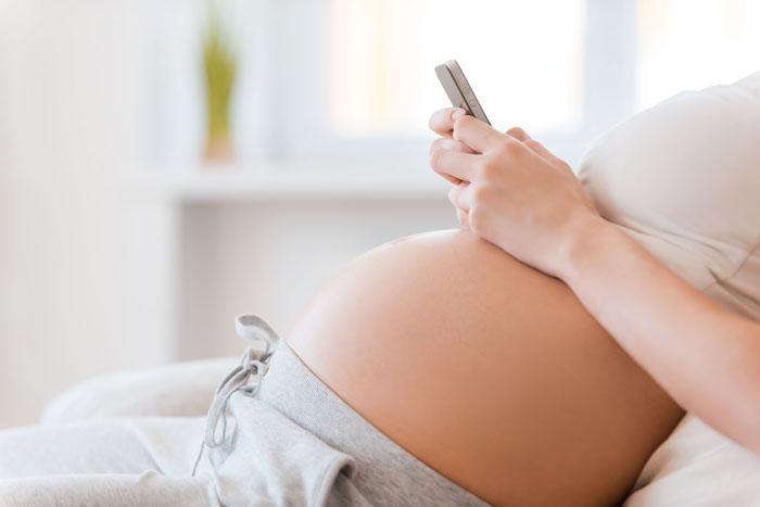Mujer embarazada tumbada en la cama mirando el móvil