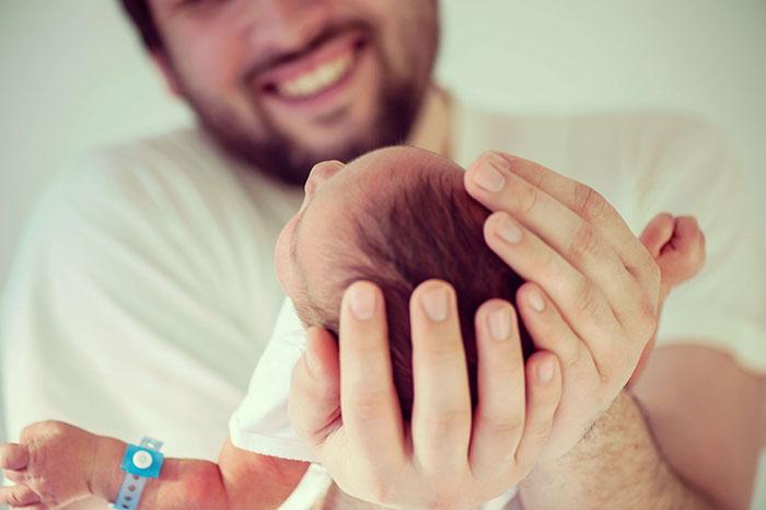 Padre sosteniendo entre sus manos la cabeza de su recién nacido
