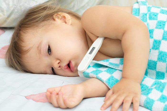 Bebé en la cama con fiebre y un termómetro en el brazo
