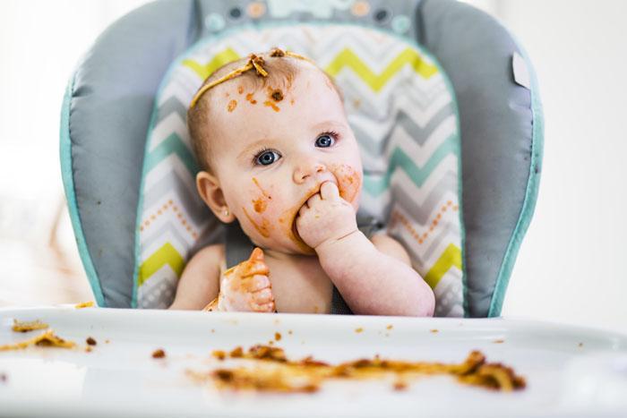 Bebé comiendo en la trona manchado de comida