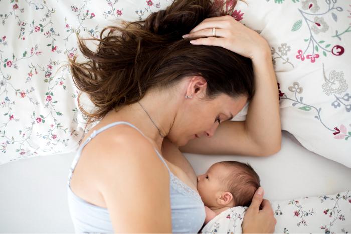 Mujer dando el pecho a su bebé acostada en la cama