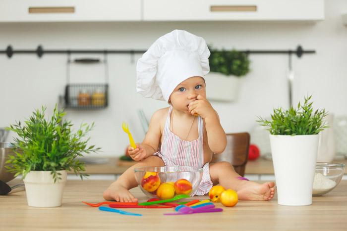 Niña con sombrero de cocinero comiendo fruta a mordiscos