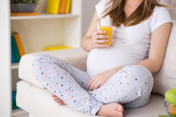 Mujer embarazada bebiendo zumo para paliar el sabor metálico en su boca