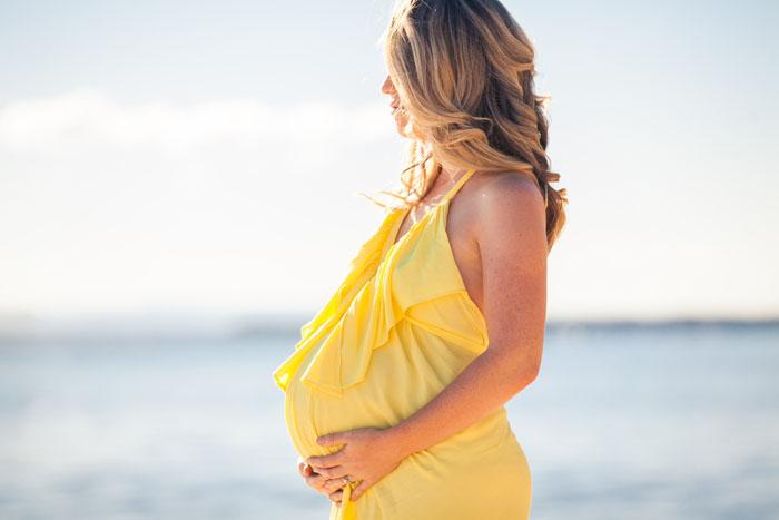 Mujer embarazada en la playa con un vestido amarillo de tirantes