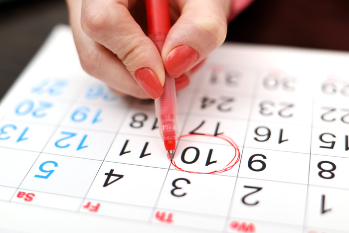 Mano de mujer marcando un día en el calendario con un rotulador rojo