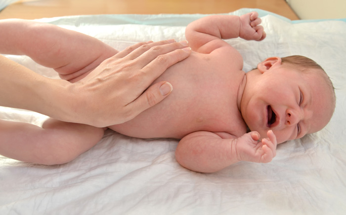 Recién nacido llorando por dolor de barriga mientras su madre le masajea