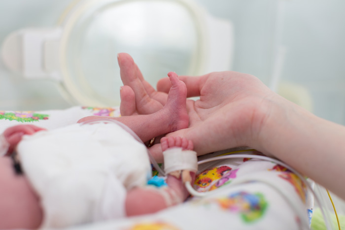 Mano de mujer sujetando el pie de un bebé prematuro en la incubadora