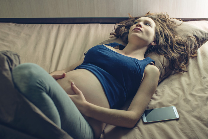 Mujer embarazada tumbada en la cama tocándose el vientre