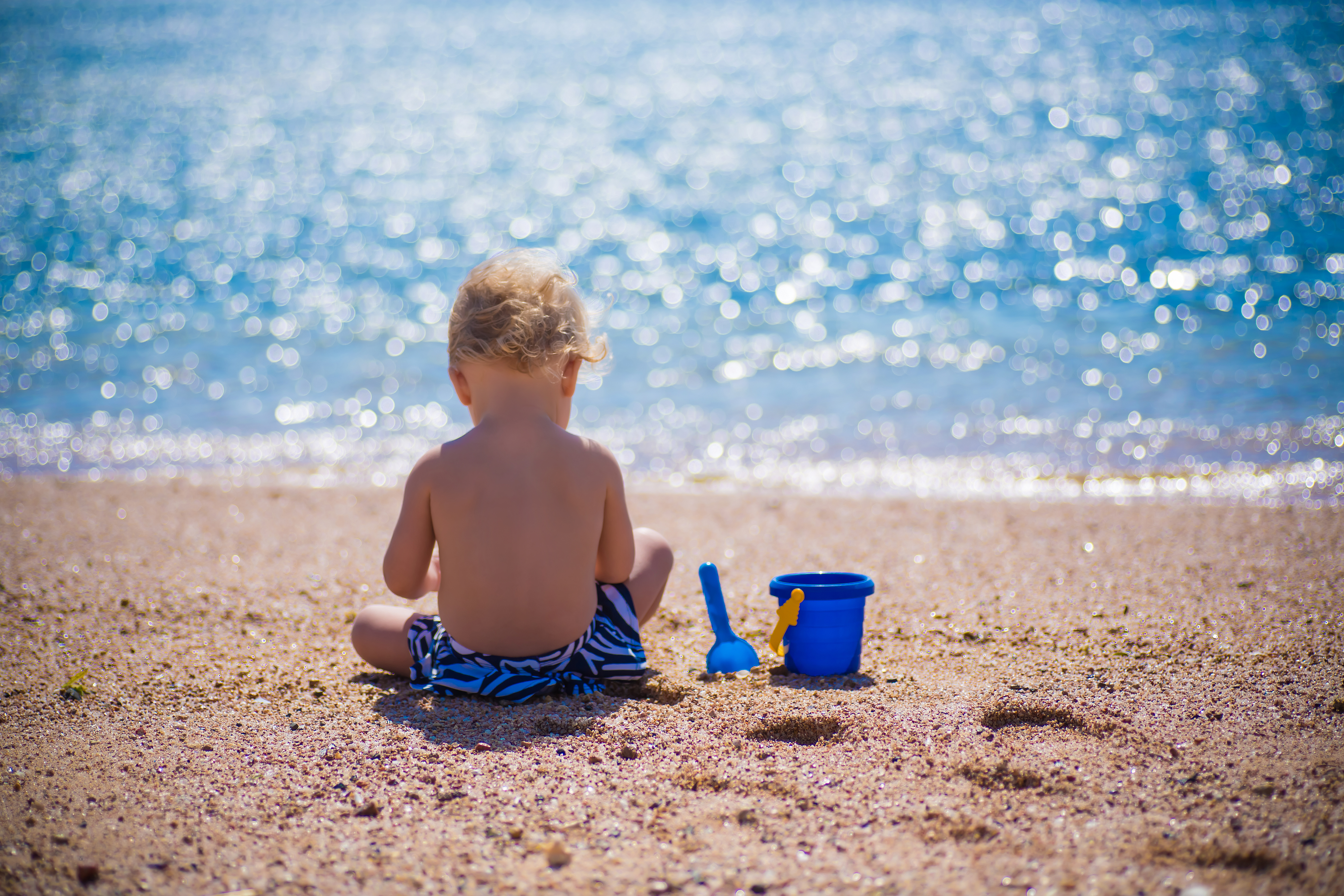 Niño jugando en la playa bajo el sol de espaldas