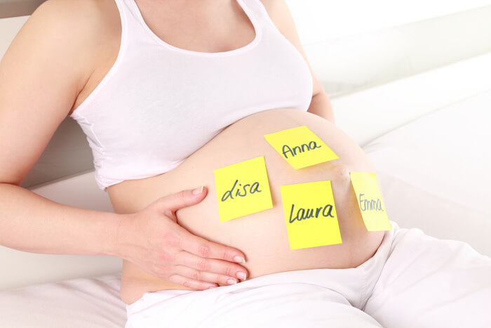 Mujer embarazada con post-its con nombres para su bebé en el vientre